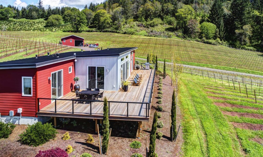 Prefab home with spacious deck overlooking vineyard, showcasing sustainable rural living design.