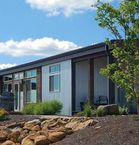 Stylish open-concept living space in a prefab home with a cozy seating area, large windows, and warm wooden finishes.