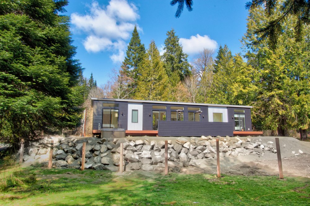 Contemporary modular home with wide front porch and floor-to-ceiling windows.