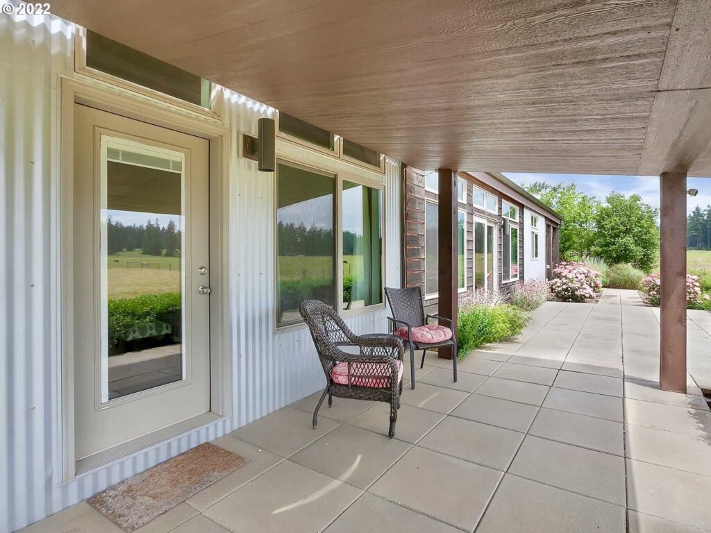Covered patio of ideabox prefab home with seating, flowers, and expansive windows.