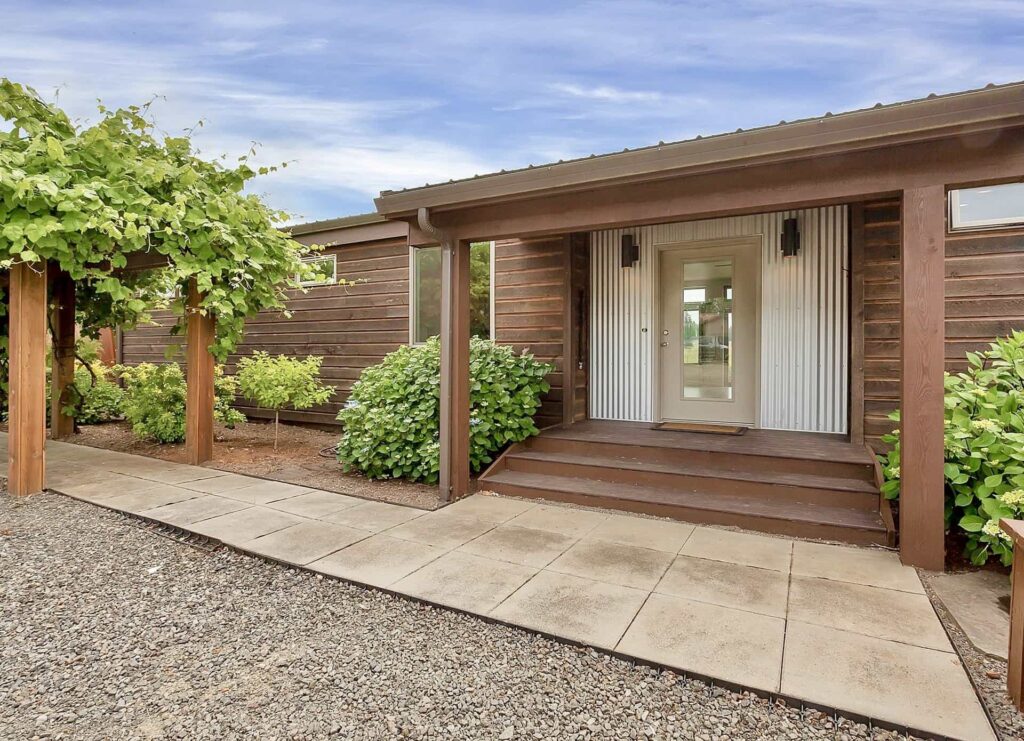 Wood-accented ideabox prefab home entry with greenery, promoting sustainable outdoor living