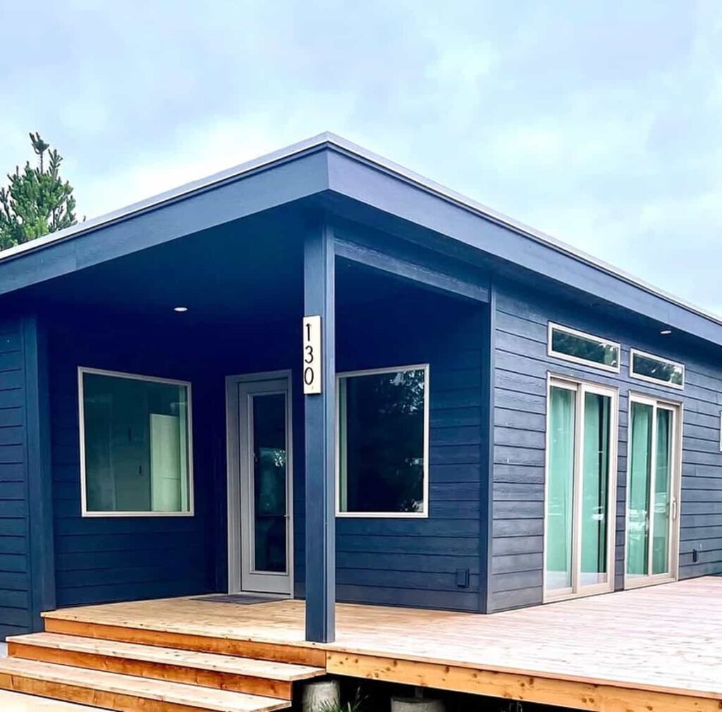 Modern blue prefab home with covered porch large windows and clean architectural lines