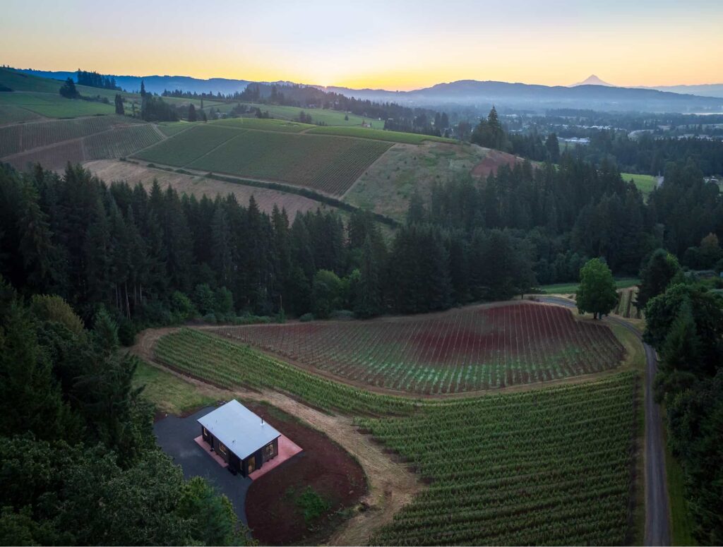 Aerial view of a modern guest cottage surrounded by vineyards and rolling hills at sunrise near Bryn Mawr Vineyards.