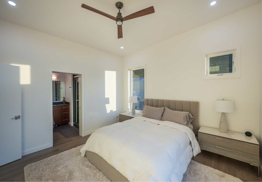 Cozy bedroom with neutral tones, a large bed, modern furnishings, and a view into a contemporary bathroom.