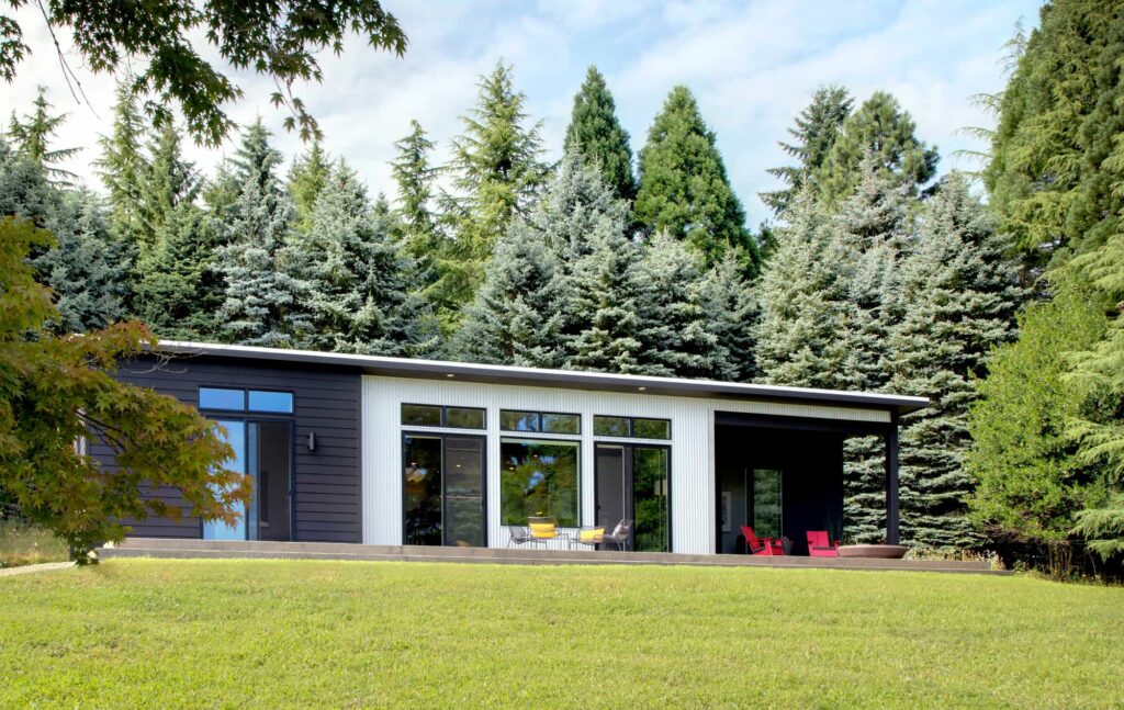 Contemporary single-story home with large windows, dark siding, and forested backdrop.