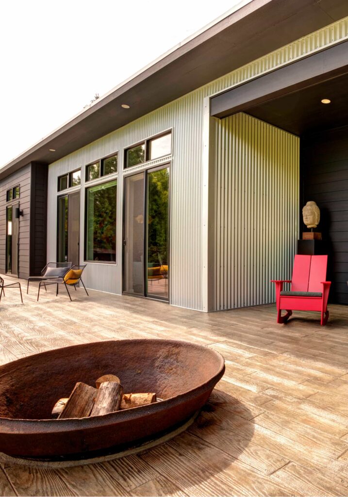 Modern home patio with wood-look decking, metal siding, red chair, and a round steel firepit.
